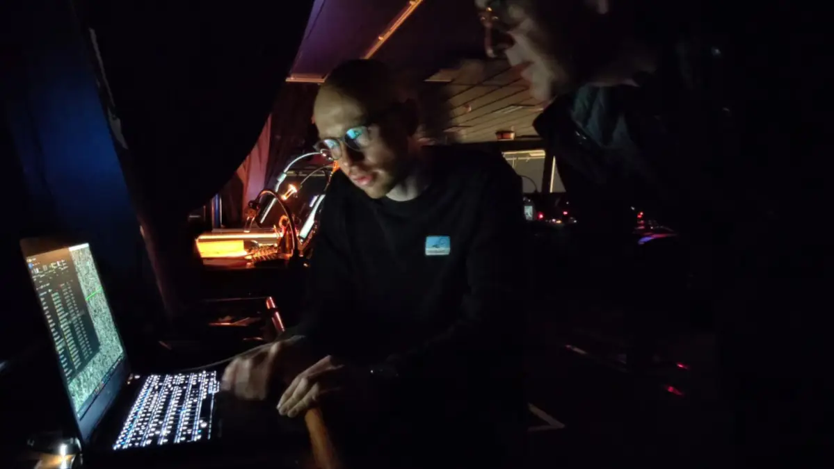Two men looking at a laptop on a dark bridge.